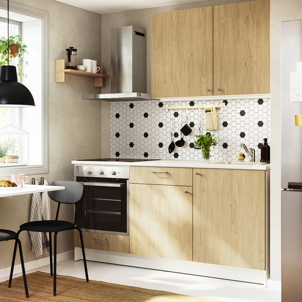 Modern kitchen with wooden cabinets, geometric tile backsplash, stainless steel appliances, small dining area, and hanging light fixture.