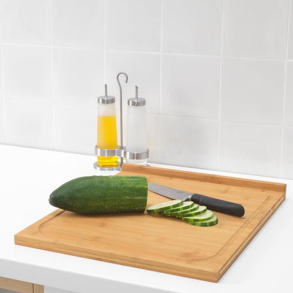 Wooden cutting board with knife and sliced cucumber; oil dispensers behind.