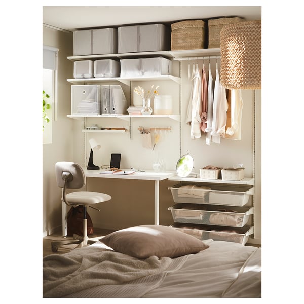 Small home office in bedroom. Desk with chair, shelves, baskets, and lamp. Beige and white decor.