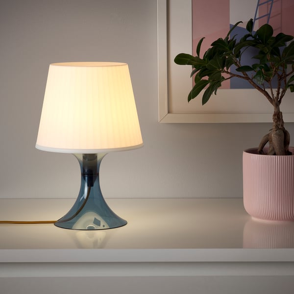 A modern lamp with a sleek base and white shade, lit and casting soft light.