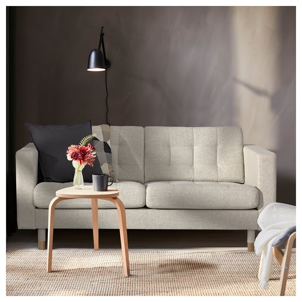 Modern living room with grey LANDSKRONA sofa, black throw pillow, wooden side table, black mug, flower vase, and floor lamp.