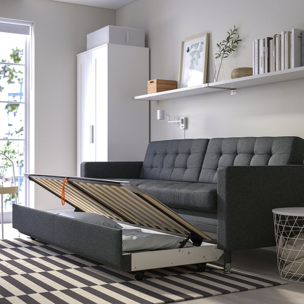 Modern grey sofa transforms into bed, revealed by lifted seat showing slats and storage.