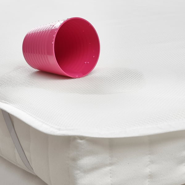 A bright pink plastic cup sits on a white mattress protector, showcasing how the mattress is kept clean and dry.