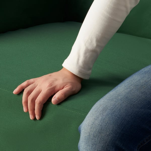 Close-up of a persons hand on a green sofa cushion, showcasing the smooth fabric and quality of the LINANÄS cover.