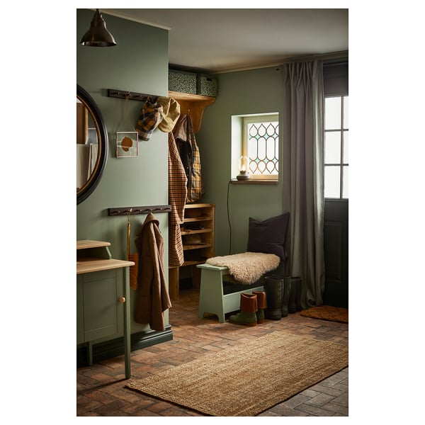 Natural jute rug in hall with coats and furniture, green walls.