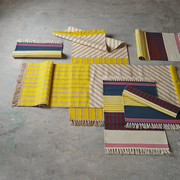 Handwoven MÄVINN rugs in yellow, blue, red on floor. Wool, jute with stripes. Vibrant colours.