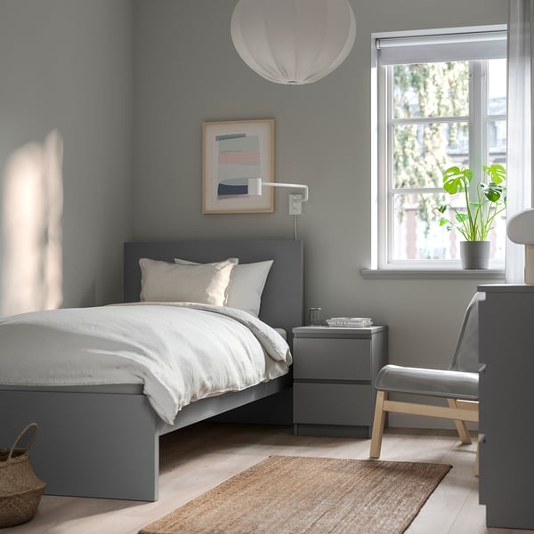 Modern grey bedroom with MALM bed, bedside table, and chair. Grey bed against window, white pillows, grey bedding, grey rug, and wall art.