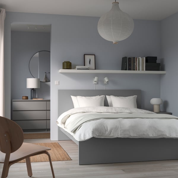Modern blue bedroom with white MALM bed, white lamps, wooden chair, grey dresser, and hanging light.
