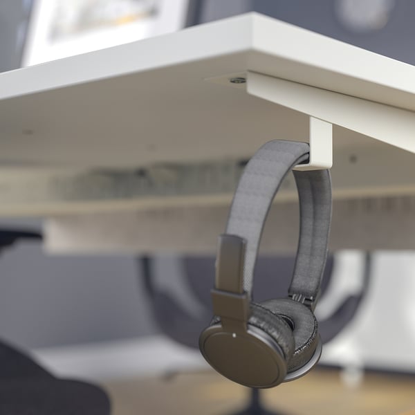 Grey headphones hang on a hook under a white desk.