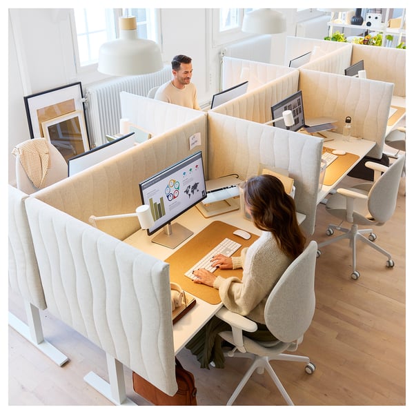 Modern office with MITTZON desks, cushioned chairs, and cream partitions. Two employees work on computers.