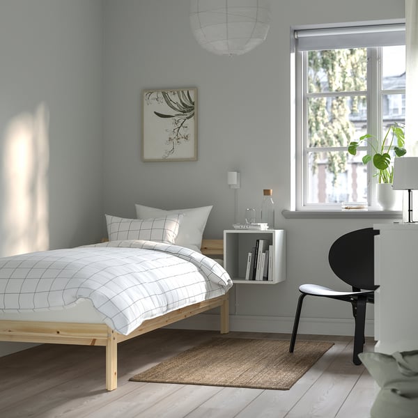 Minimalist bedroom with white bed, blue walls, plants, books, black chair, large window.