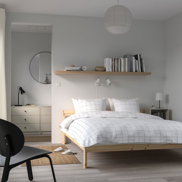 Modern minimalist bedroom with grid-patterned bed, wooden frames, and large mirror.