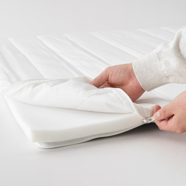 Person zips up white mattress pad with cover on a bed.