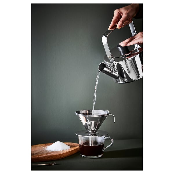 Pouring water into coffee maker over mug on green surface, sugar nearby.
