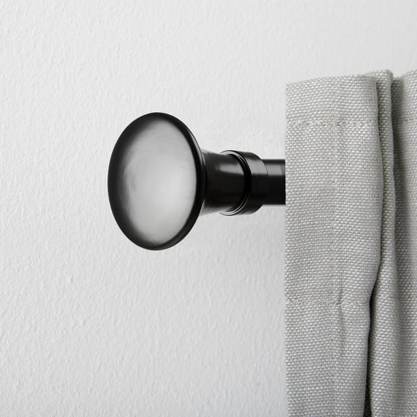 Black curtain rod finial with trumpet shape, holding light grey curtain against white wall.