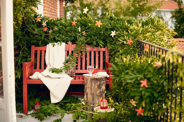 Red acacia wooden bench with back curve, white blanket, outdoor garden setting.