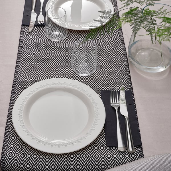 Table set with two plates, cutlery, and glasses on patterned placemats.