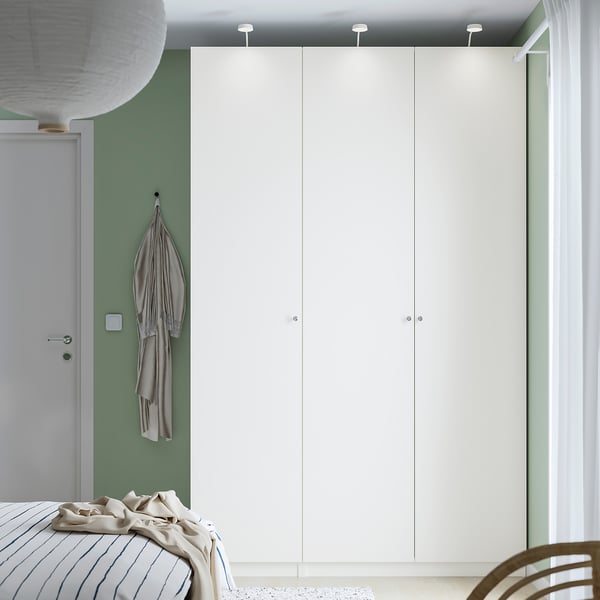Modern room with PAX wardrobe, beige bed linens, and a hanging garment. Minimalist style with green walls.