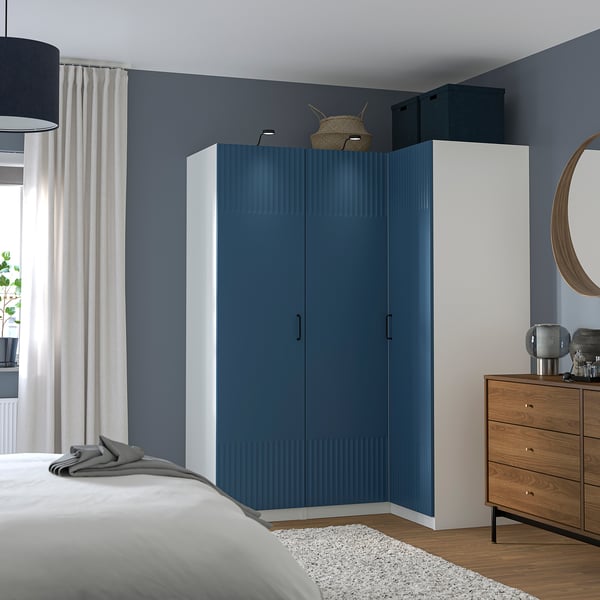 Modern bedroom with blue and white wardrobe, wooden chest, round mirror, and a bed with white linens.
