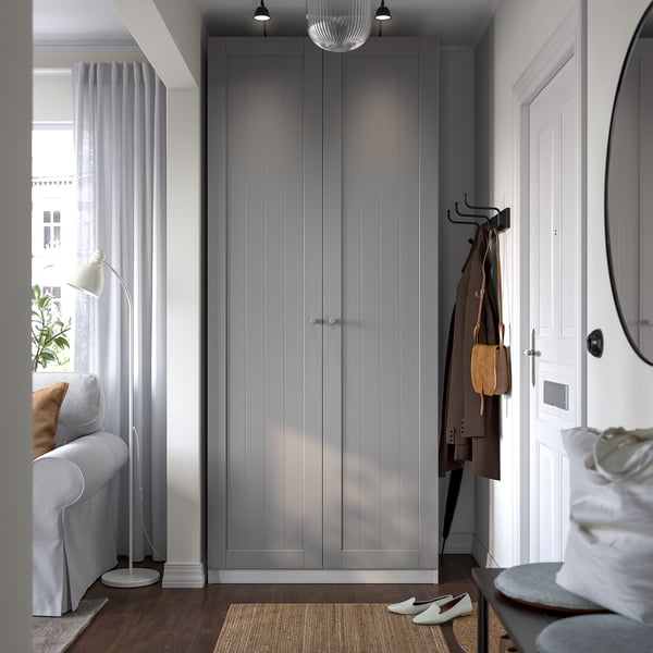 Modern entryway with IKEA PAX wardrobe, coat hooks, grey sofa, and floor lamp.