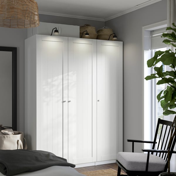 Modern white corner wardrobe with wicker baskets, window, plant, cosy chair.