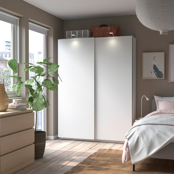 Modern bedroom with white PAX wardrobe, wooden floor, bed, plant, and artwork.
