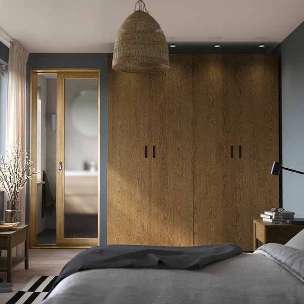 Modern bedroom with wooden wardrobe, grey bedding, and hanging light, framed by a large mirror.