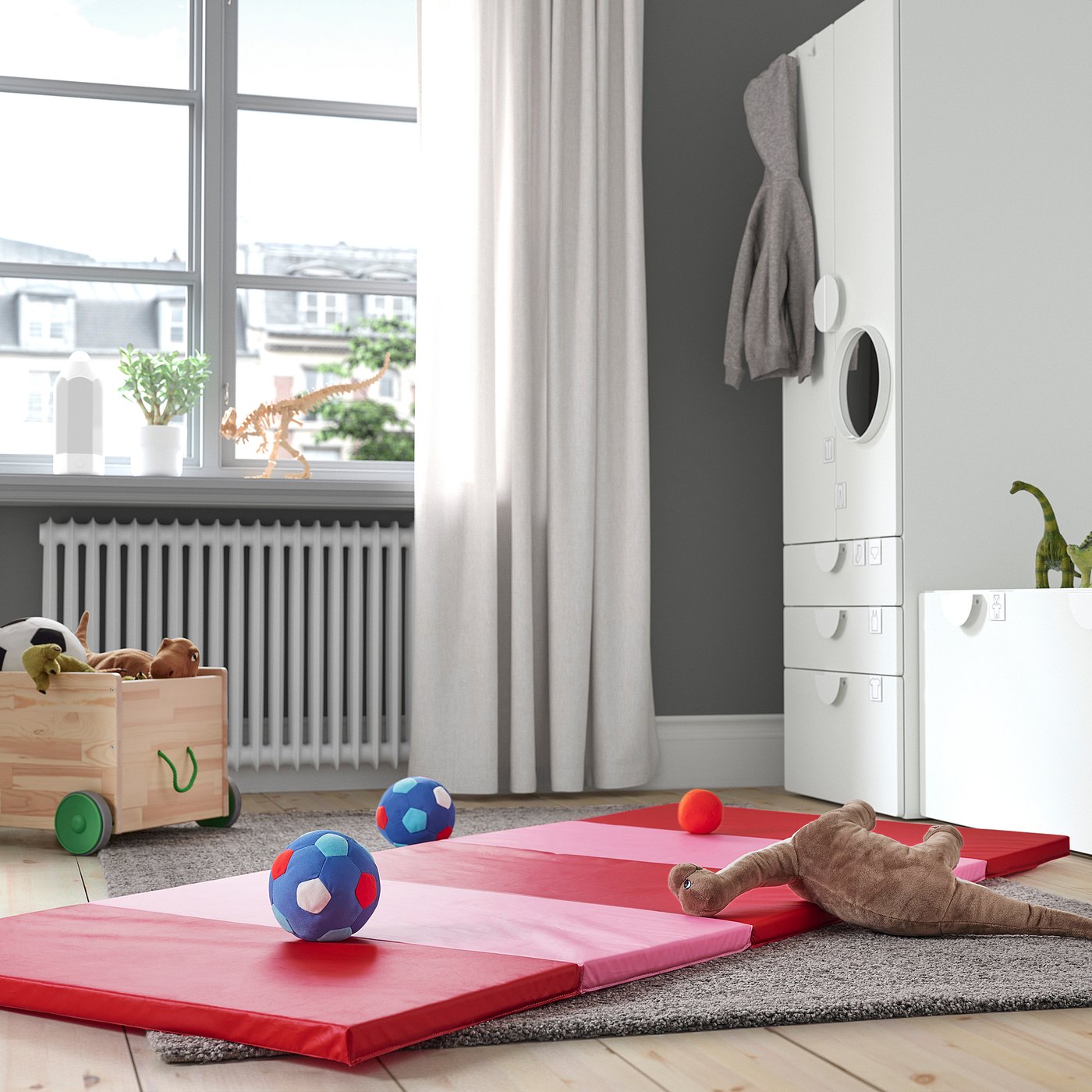 Kids room with red/pink PLUFSIG gym mats, soft peva/polyester, rug, white radiator, window curtains, wooden toy box.