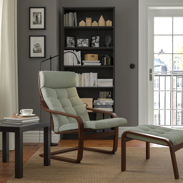 Green POÄNG chair next to bookshelf with cup, books, and footstool. Cosy, minimalist room with natural light.