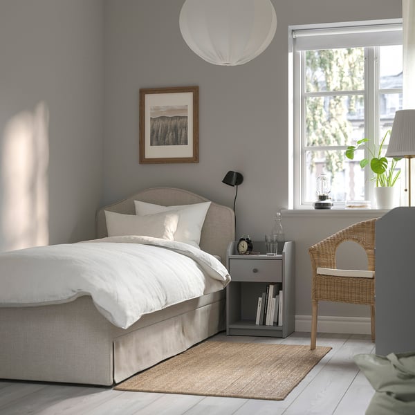 Beige RAMNEFJÄLL bed, grey bedside table, wicker chair, tree view.