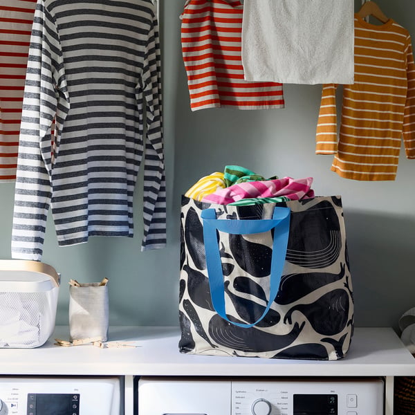ROMELSÖN bag, blue, patterned, sits on washer, holds colourful cloths, surrounded by striped shirts.