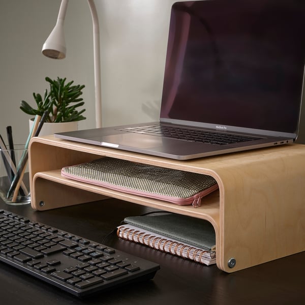 ROMELSÖN wooden laptop stand, light brown, curved design, holds laptop high, keyboard fits underneath, small plant and pens nearby.