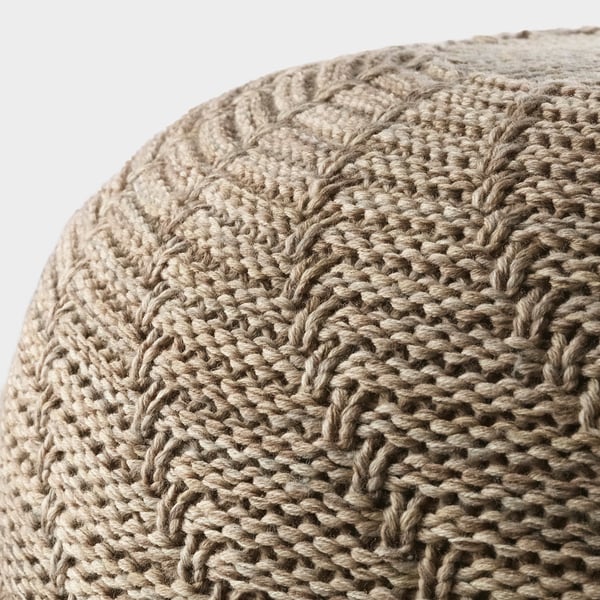 Close-up of a knitted pouffe in neutral tones, showcasing its soft, textured surface and intricate pattern. High-quality, hand-crafted texture detail.
