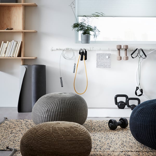 Home gym with SANDARED pouffes in beige and grey, knitted textures, dumbbells, resistance bands, yoga mat, and plants.