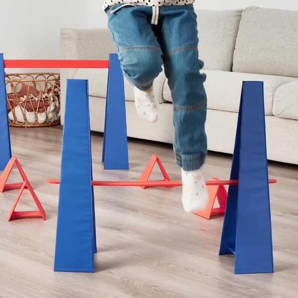 A child jumping over blue and red obstacle course hurdles, promoting physical activity and motor skill development.
