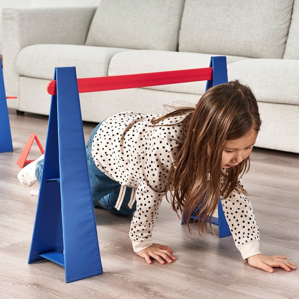 Child crawling under red-blue obstacle course hurdle.