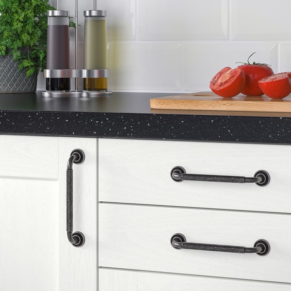 Modern kitchen with black-speckled counters, white cabinets with dark handles, and fresh herbs.