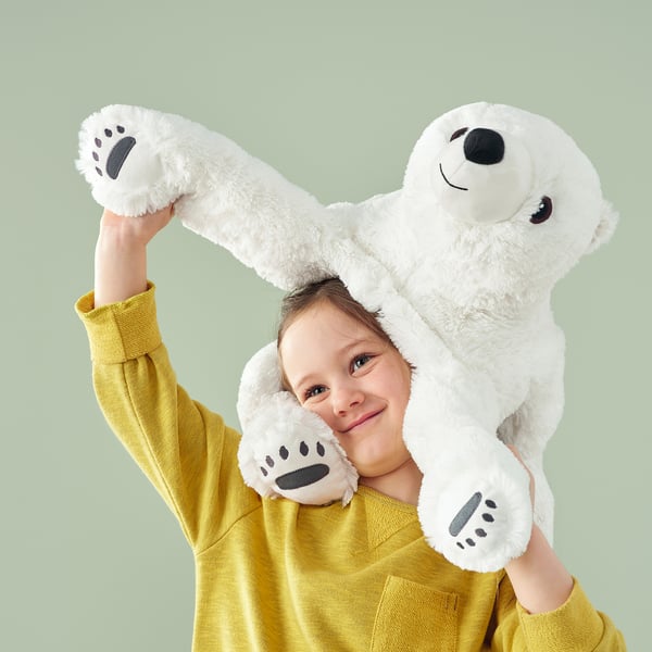 Child in yellow sweater holding large white plush polar bear above head, both smiling.