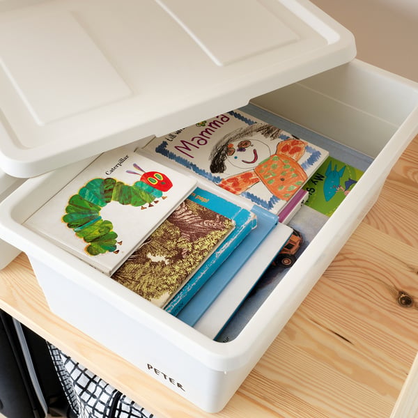 Open plastic storage box filled with childrens books and a small toy on a light wooden surface.