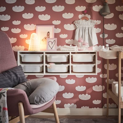 Nursery corner with cloud wallpaper, SOLBO lamp, storage, baby dress, and cushioned chair.