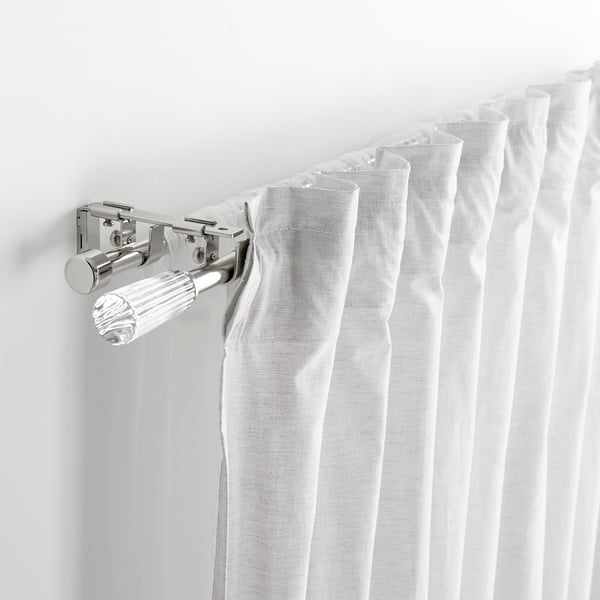 Close-up of chrome curtain rod bracket holding white curtains, showcasing part of soldvärm set.