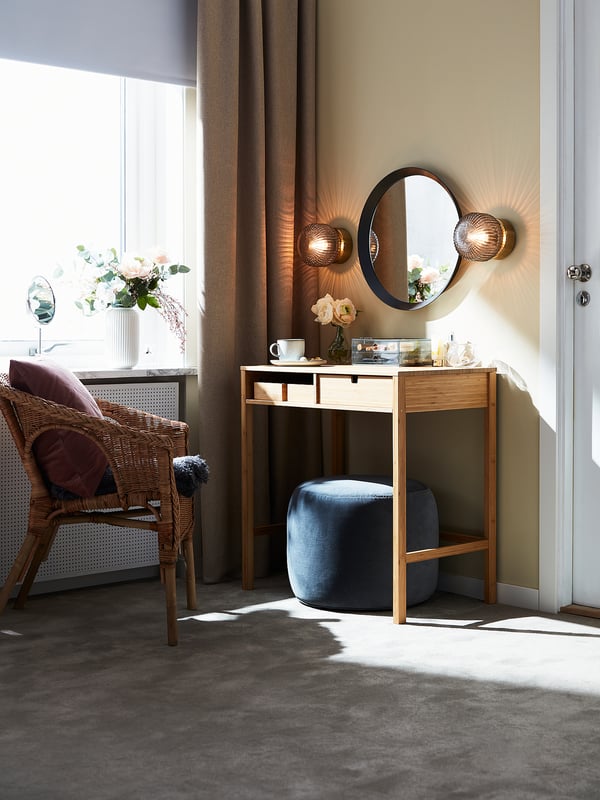 Luxurious bedroom with wicker chair, maroon pillows, vanity, round mirror, and SOLKLINT lamps.