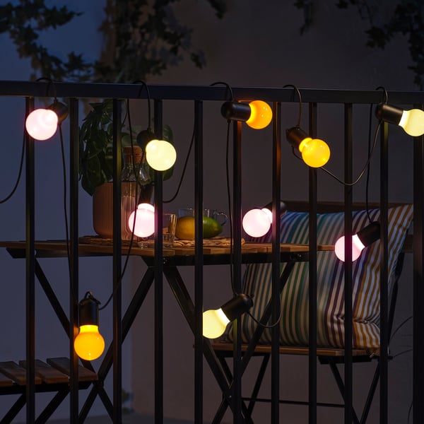 String lights hang across a balcony, illuminating with warm yellow and soft pink hues, ideal for outdoor use, casting a cosy ambiance.