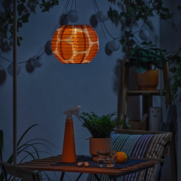 Orange lantern illuminates cosy patio with plant, glassware, and lemon. Stripes and cushions add to relaxed ambiance.