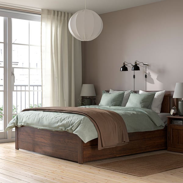 Modern bedroom with brown SONGESAND bed, light green linens, large window, hanging lamp, nightstands.