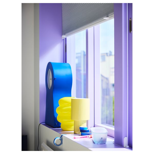 Bright blue SPETSBOJ clock on window sill, small and colourful, surrounded by vibrant items.