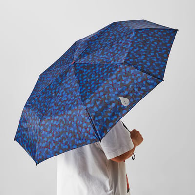 Person holding open a blue patterned SPJUTSÖ umbrella, providing rain protection.