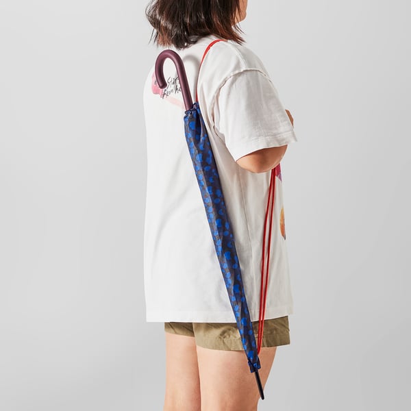 Person holding an umbrella with a blue dotted pattern. The umbrella is closed and slung over their shoulder.