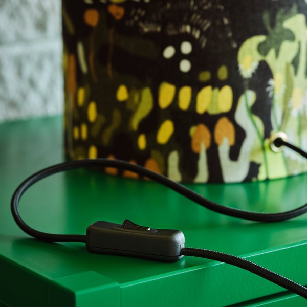 Black corded switch on green surface beside patterned lamp.