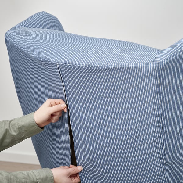 Person placing blue striped slipcover on chair, showing practical and easy-to-use design.